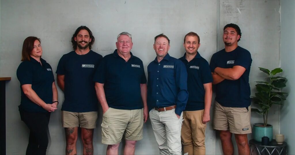 The CKS Projects team: six people in navy CKS shirts standing against a concrete wall